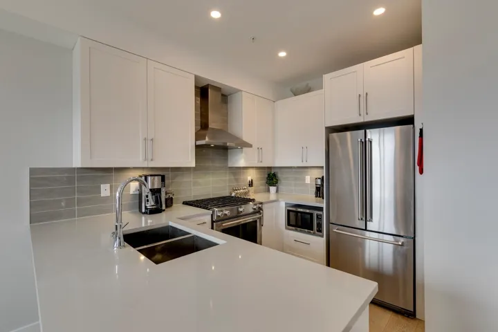 Kitchen with appliances with stainless steel finishes, wall chimney range hood, white cabinets, decorative backsplash, and recessed lighting