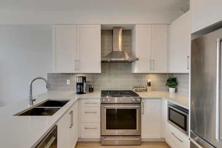Kitchen with stainless steel appliances, wall chimney exhaust hood, tasteful backsplash, and white cabinetry