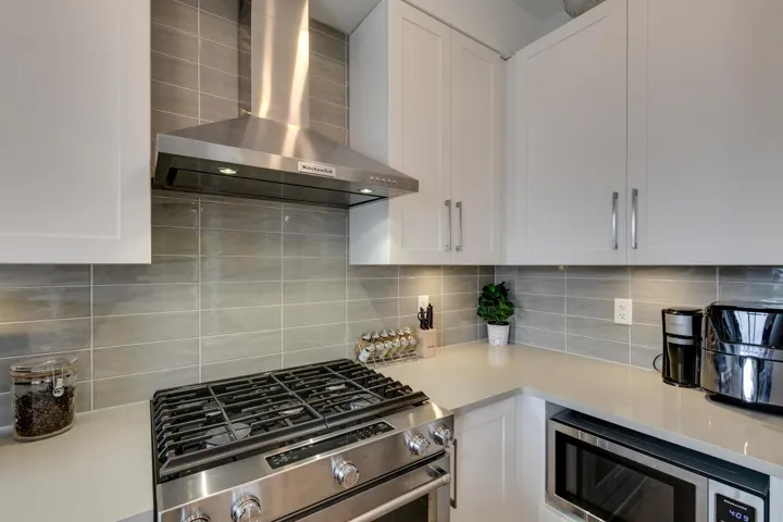 Kitchen featuring wall chimney exhaust hood, stainless steel appliances, white cabinets, and decorative backsplash