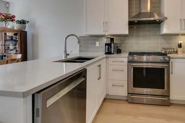 Kitchen with stainless steel appliances, wall chimney exhaust hood, white cabinets, tasteful backsplash, and a peninsula