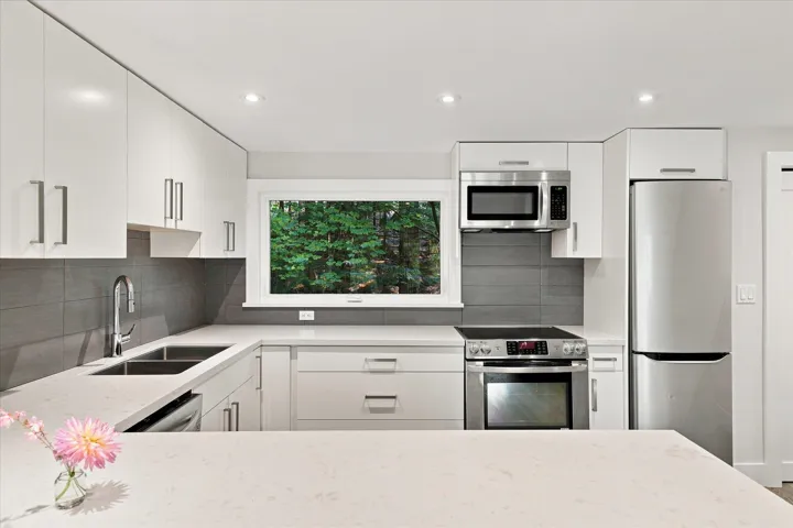 Kitchen featuring white cabinetry, stainless steel appliances, a double basin sink, light-toned countertops, and a tile backsplash