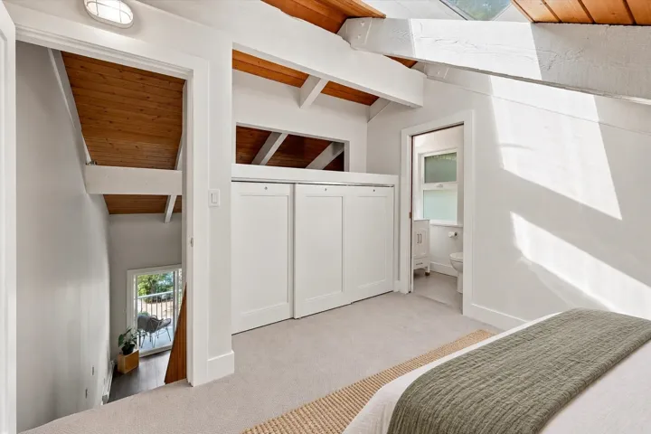 Vaulted wood-paneled ceilings with exposed beams, light-colored carpeting, white sliding wardrobe doors, a skylight, and a white vanity with a rectangular sink