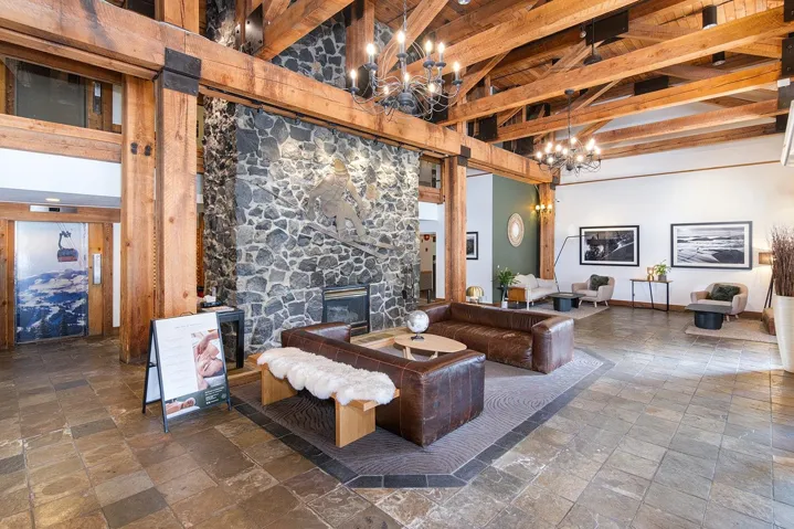 Living room featuring a stone fireplace, suspended lighting, stone tile floors, and a high wooden beamed ceiling