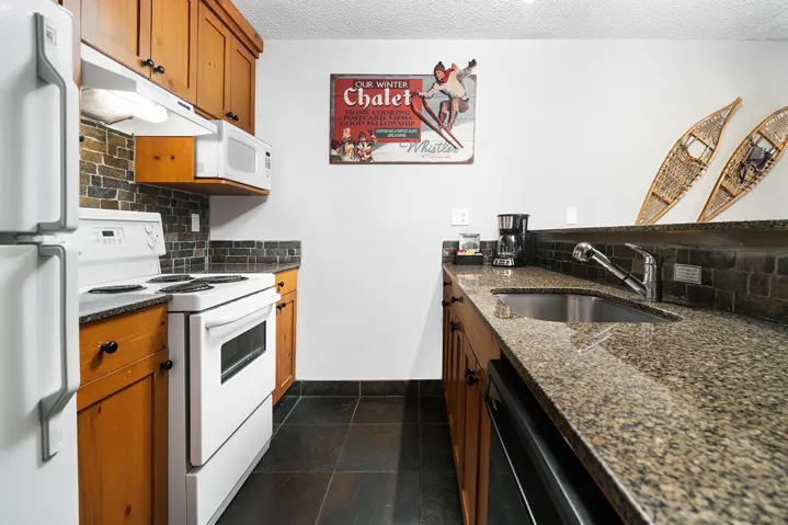 Kitchen with tasteful backsplash, white appliances, wood finish cabinets, dark stone counters, and a textured ceiling