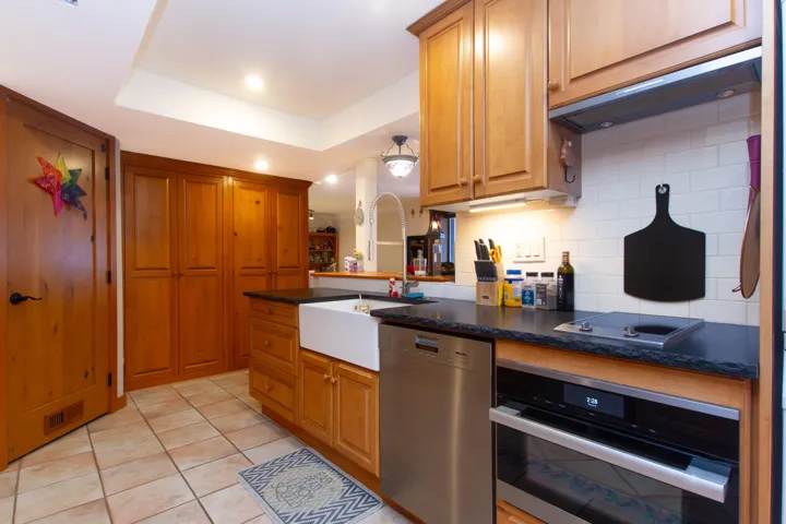 Kitchen featuring light tile patterned flooring, a sink, appliances with stainless steel finishes, decorative backsplash, and dark countertops