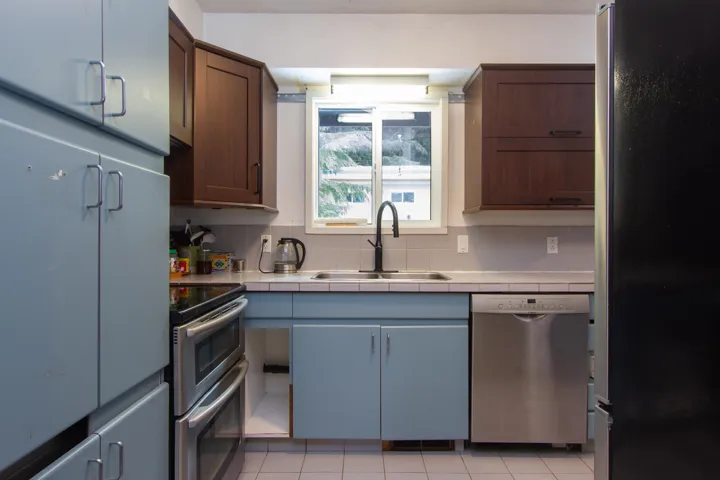Kitchen with tile counters, appliances with stainless steel finishes, decorative backsplash, and a sink