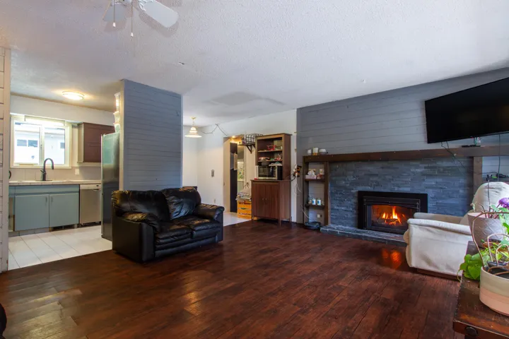 Living room with light wood-style floors, a stone fireplace, a textured ceiling, and a ceiling fan
