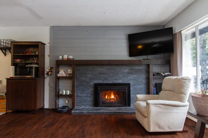 Living area featuring a textured ceiling, a stone fireplace, and wood finished floors