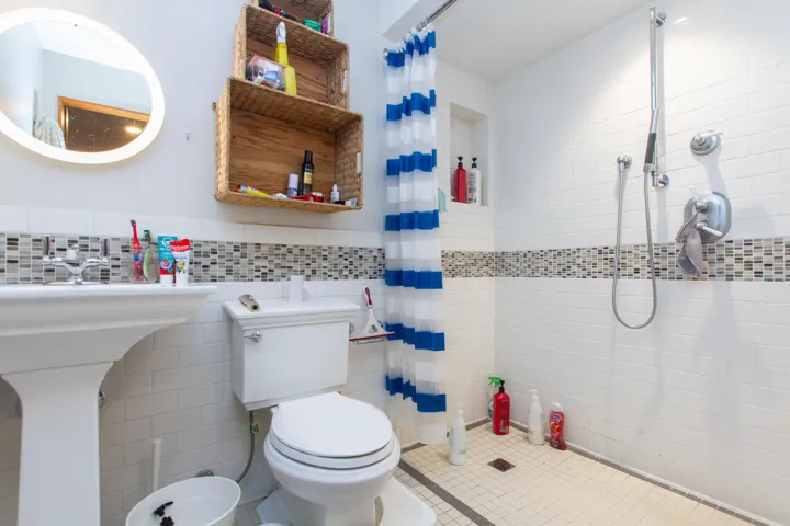 Full bath featuring toilet, a wainscoted wall, a tile shower, and tile walls