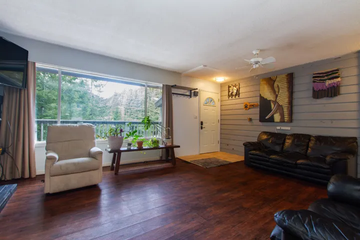 Living area with a textured ceiling, wooden walls, a ceiling fan, and wood finished floors