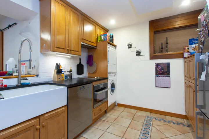 Kitchen featuring light tile patterned flooring, stainless steel appliances, stacked washer / dryer, a sink, and decorative backsplash