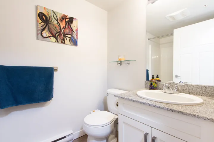 Bathroom featuring visible vents, a baseboard heating unit, walk in shower, toilet, and vanity