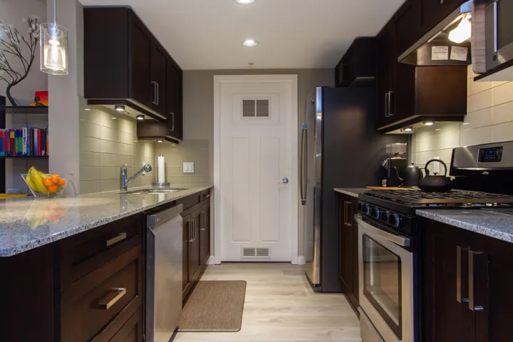 Kitchen featuring under cabinet range hood, light stone counters, light wood-style flooring, stainless steel appliances, and a sink