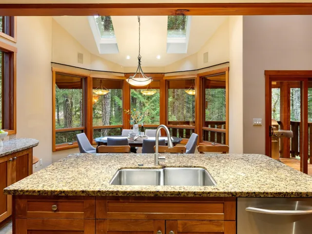 Kitchen featuring light stone counters, vaulted ceiling, pendant lighting, healthy amount of natural light, and brown cabinets