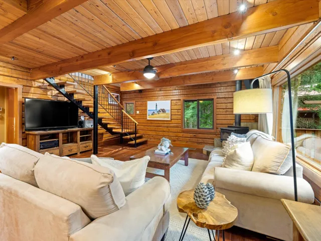 Living room with a wood stove, stairs, wooden walls, hardwood / wood-style floors, and a wood ceiling with exposed beams