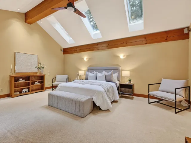 Carpeted bedroom featuring beam ceiling, a skylight, high vaulted ceiling, and ceiling fan