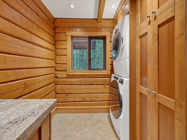 Laundry room with wood walls, estacked washer and dryer, and beam ceiling