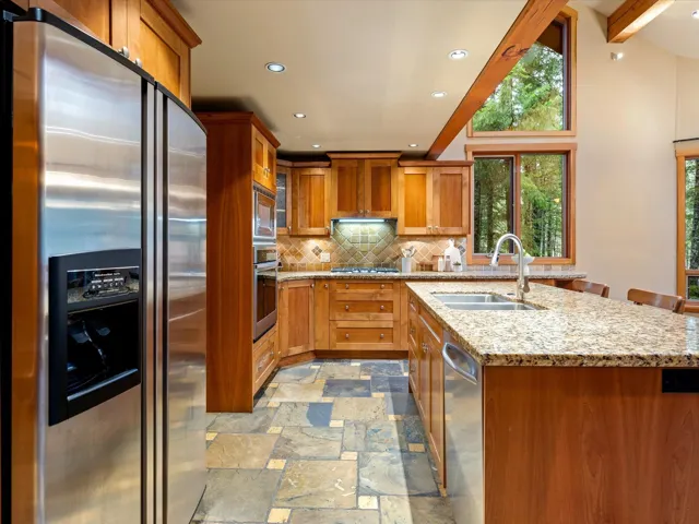 Kitchen featuring appliances with stainless steel finishes, brown cabinets, light stone counters, recessed lighting, and tasteful backsplash