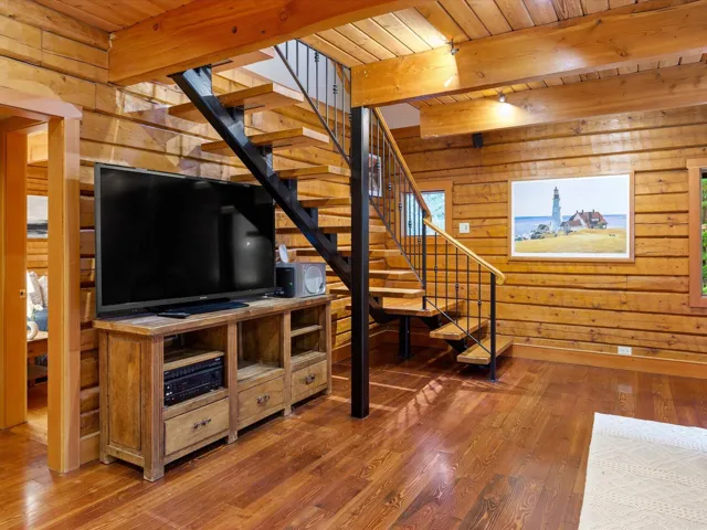 Unfurnished living room with stairway, wood walls, hardwood / wood-style floors, and a wood ceiling with exposed beams