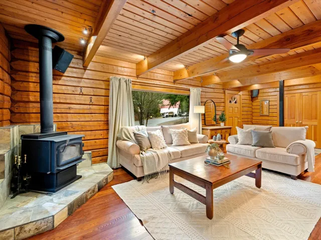 Living room featuring a wood stove, hardwood / wood-style floors, wooden walls, and a wooden ceiling with exposed beams