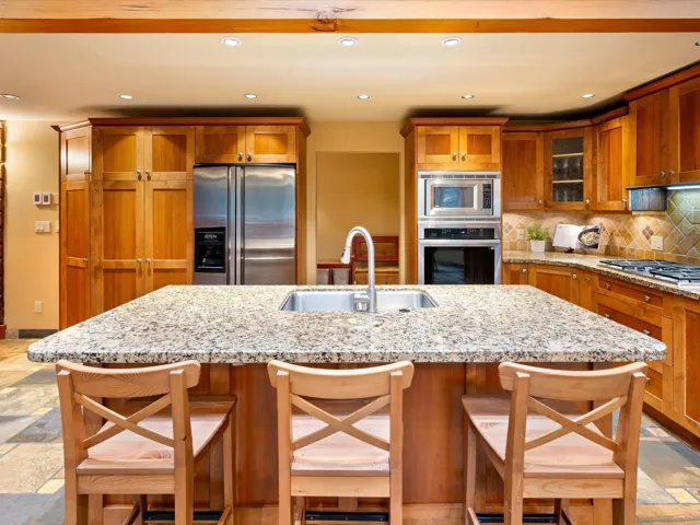 Kitchen featuring stone tile flooring, brown cabinetry, stainless steel appliances, a breakfast bar, and recessed lighting
