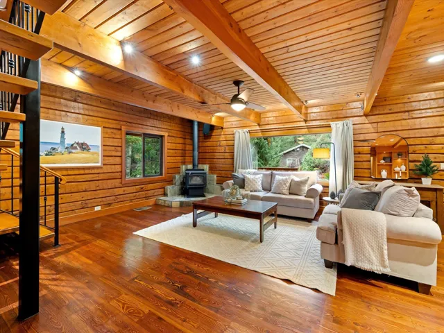 Living room with a wood stove, wood walls, wood-type flooring, stairway, and a ceiling fan