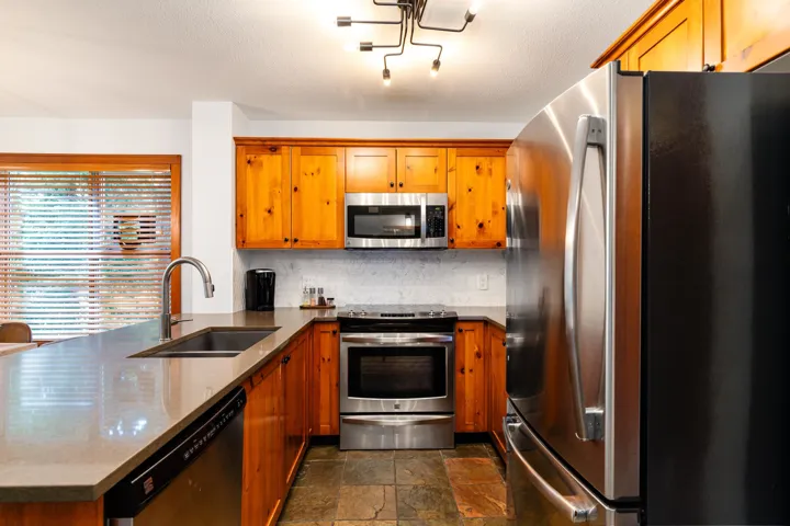 Kitchen with stainless steel appliances, a peninsula, dark stone countertops, brown cabinets, and a textured ceiling