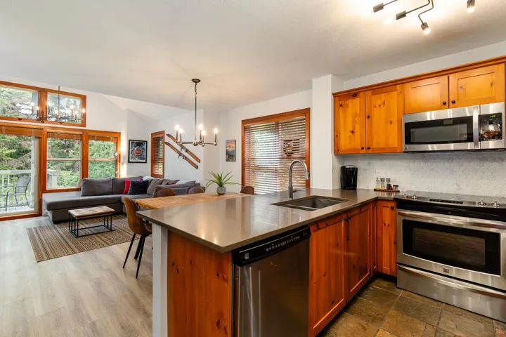 Kitchen with stainless steel appliances, brown cabinets, decorative backsplash, a peninsula, and a chandelier