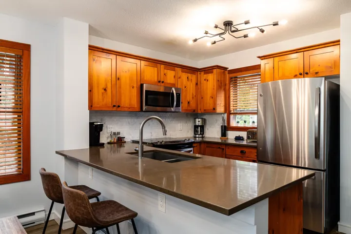 Kitchen featuring appliances with stainless steel finishes, dark stone countertops, brown cabinets, tasteful backsplash, and a breakfast bar area