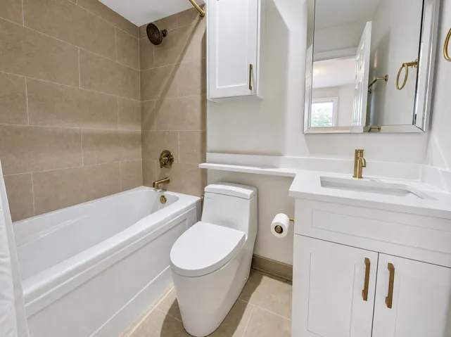 Bathtub with tile surround, white vanity with integrated sink, gold-finish fixtures, and a mirrored medicine cabinet