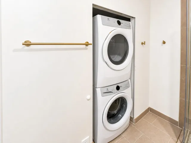 Built-in stacked washer and dryer unit, complemented by a gold-finish towel bar and wall hooks