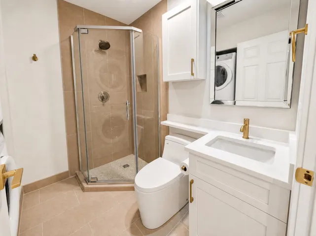 Full bathroom featuring a glass-enclosed shower, white vanity with an integrated sink, gold-tone fixtures, and a wall-mounted medicine cabinet