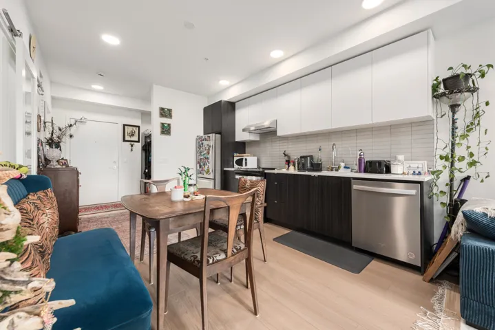 Contemporary kitchen featuring an integrated refrigerator, stainless steel dishwasher, modern range hood, and light wood-finish flooring