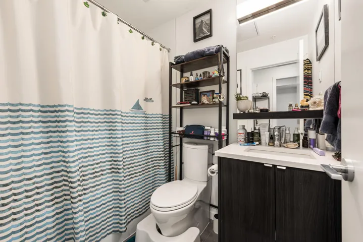 Modern bathroom featuring a dark wood-finish vanity with an integrated white sink, a wall-mounted mirror, and a contemporary toilet