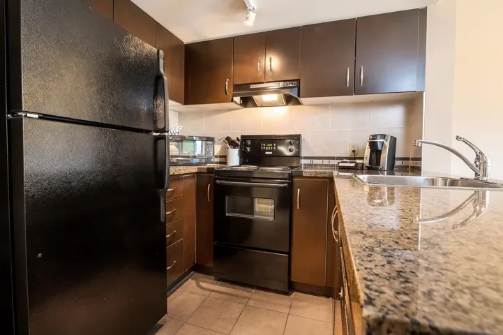 Kitchen with light tile patterned floors, a sink, black appliances, under cabinet range hood, and tasteful backsplash