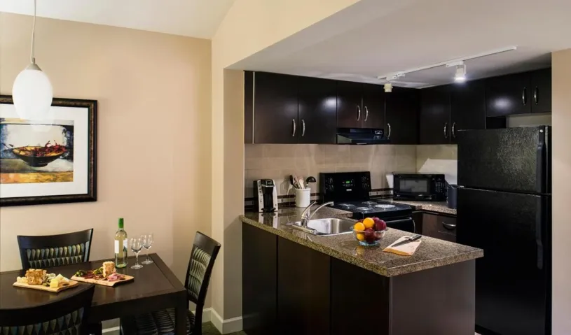 Kitchen featuring backsplash, under cabinet range hood, a peninsula, dark cabinetry, and black appliances
