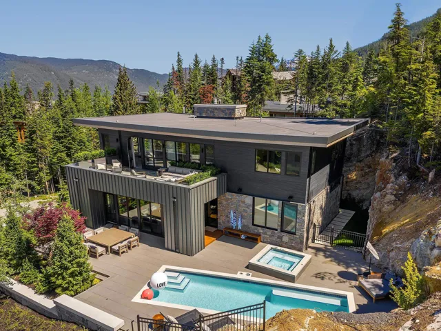 Back of house featuring an outdoor hot tub, a patio area, stone siding, a mountain view, and a balcony