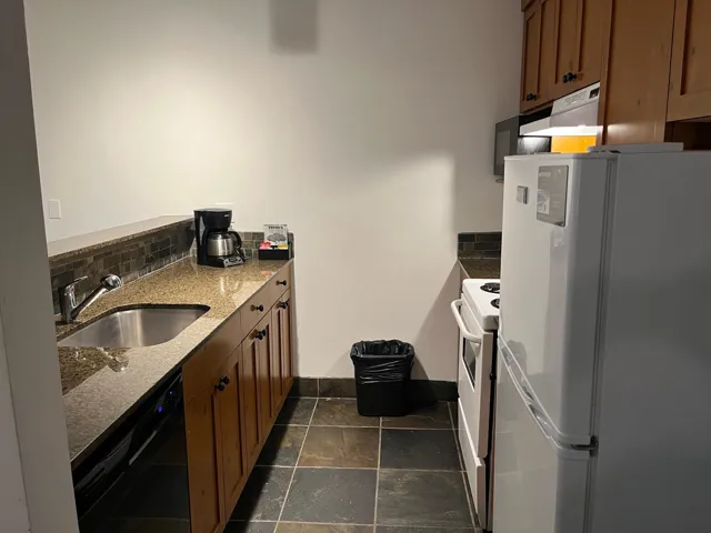 Kitchen featuring white appliances, wood finish cabinets, dark stone countertops, decorative backsplash, and dark stone finish floors