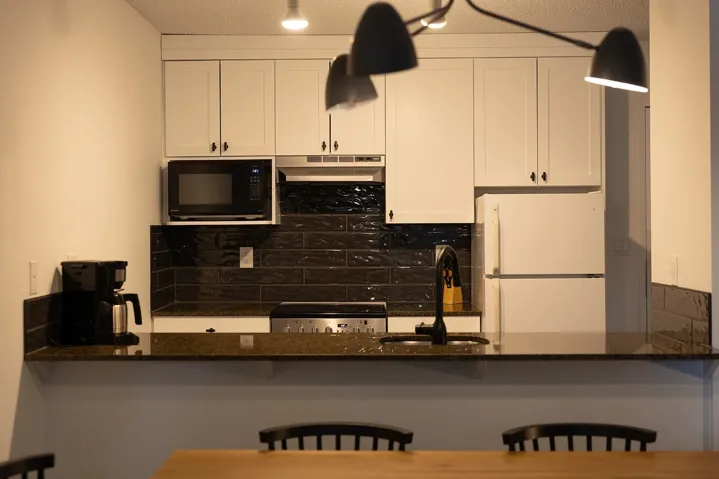 Kitchen with a peninsula, a kitchen breakfast bar, freestanding refrigerator, dark stone countertops, and backsplash