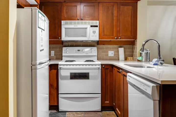 Kitchen with white appliances, light countertops, a sink, and a peninsula