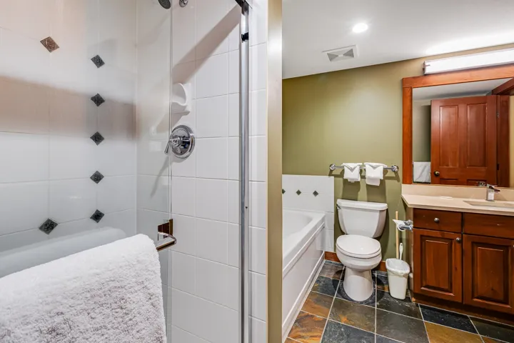 Bathroom with stone tile floors, visible vents, toilet, a tile shower, and vanity
