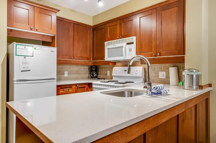 Kitchen with light stone counters, white appliances, brown cabinets, and a sink