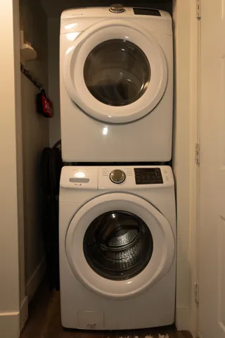 Clothes washing area with stacked washer and clothes dryer and dark wood-style flooring
