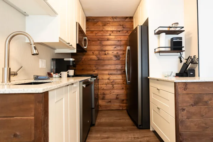 Kitchen with appliances with stainless steel finishes, a sink, dark wood finished floors, white cabinets, and wooden walls
