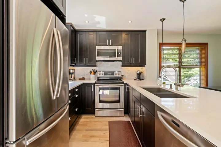 Kitchen featuring stainless steel appliances, light wood-type flooring, light countertops, tasteful backsplash, and decorative light fixtures