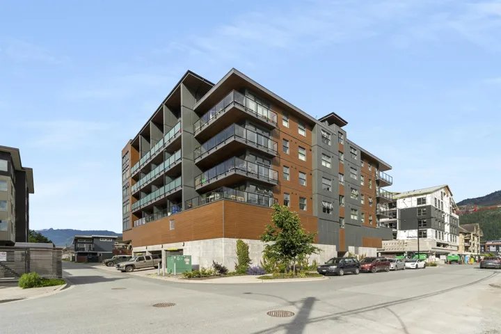 Multi-story building featuring modern exterior cladding, multiple private balconies with glass railings, and a concrete foundation