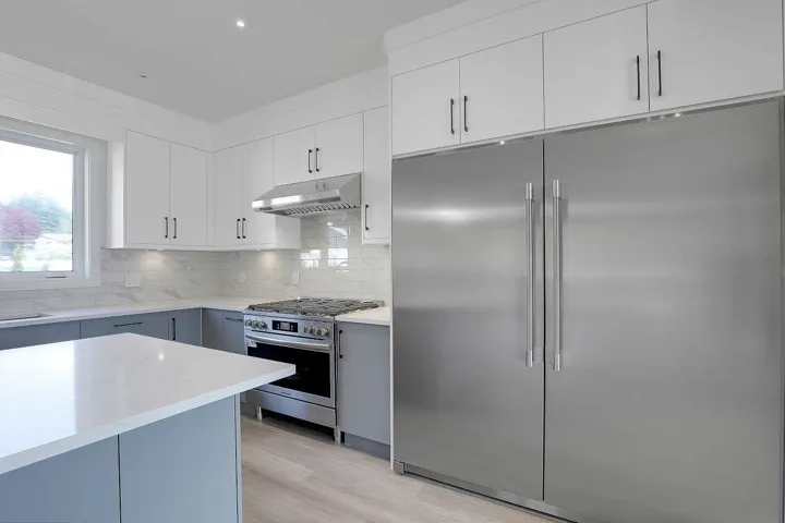 Kitchen featuring appliances with stainless steel finishes, gray cabinetry, decorative backsplash, light wood finished floors, and light stone counters