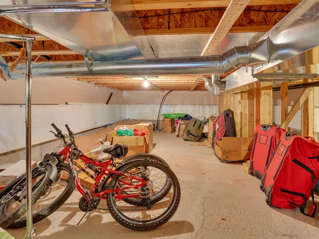 Unfinished basement space featuring exposed wood joists and structural beams, visible galvanized ductwork, concrete flooring, and perimeter wall framing