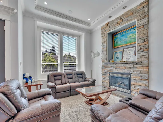Living area featuring a stone-clad fireplace with mantel, recessed lighting, decorative crown molding, and large windows