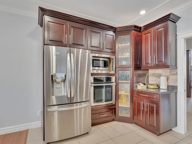 Kitchen featuring dark wood-finish cabinetry with crown molding, stainless steel appliances, and a tiled backsplash